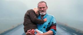 A man with a salt and pepper beard carrying a young blond girl in his arms. 