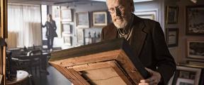A man looking down at an old wooden picture frame.
