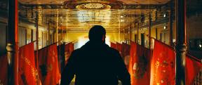 Shot of a man's back as he looks over a room with flags hanging from the wall.